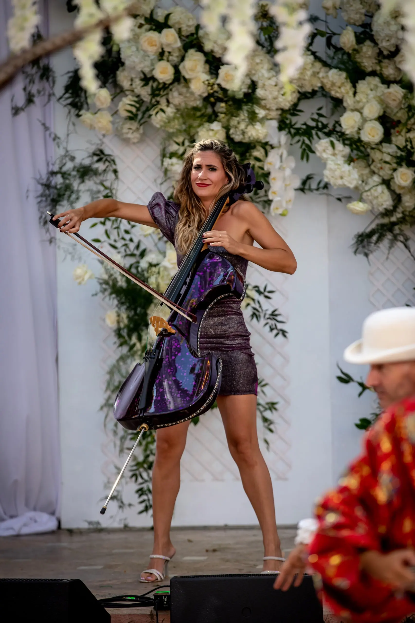 An electric cellist performing in front of a white floral arch