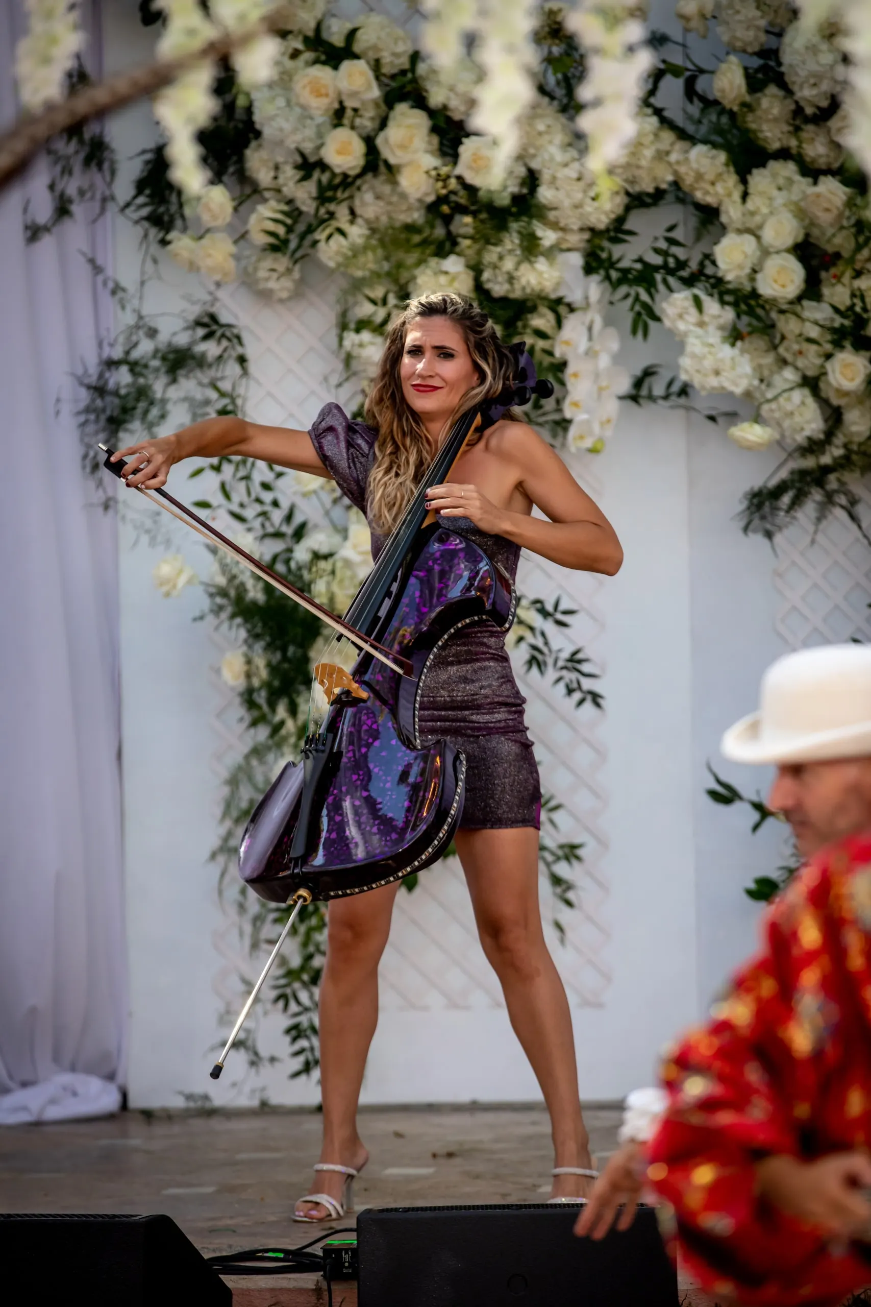An electric cellist performing in front of a white floral arch during a wedding drinks reception