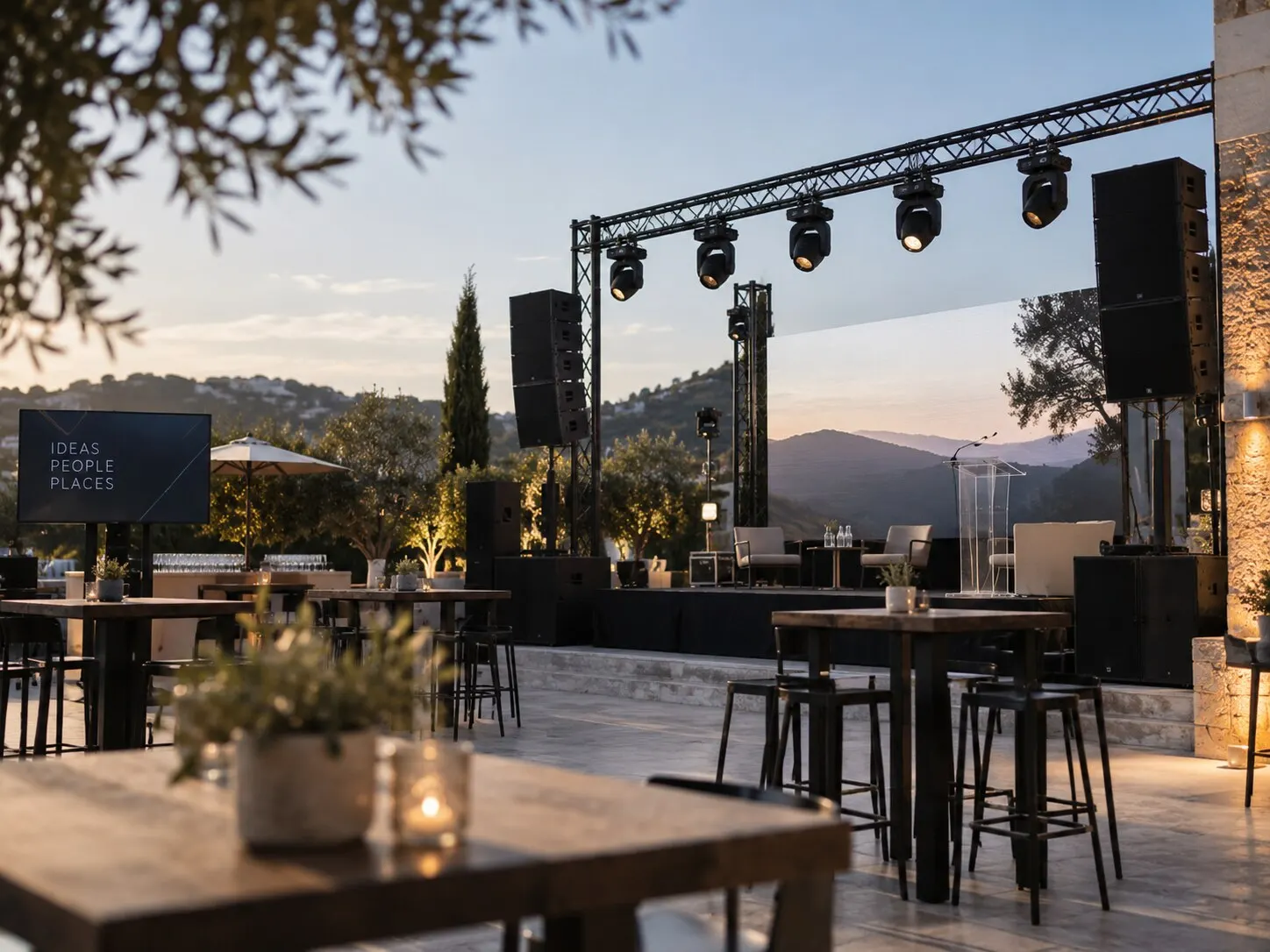 A corporate event on a terrace at dusk with a stage, lectern, presentation screen and cocktail tables