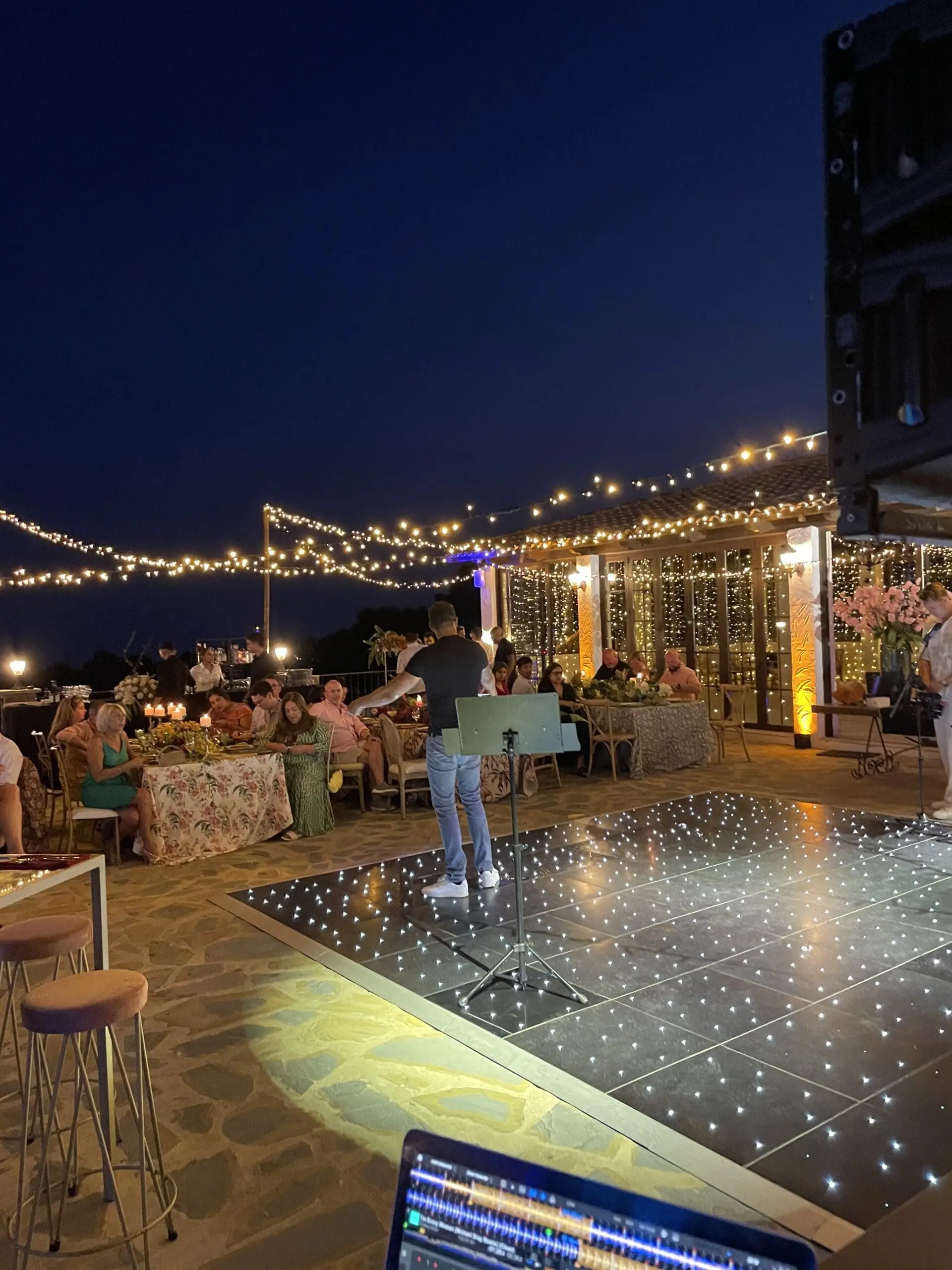 A lit dancefloor with bar stools and festoon lighting at a private evening party