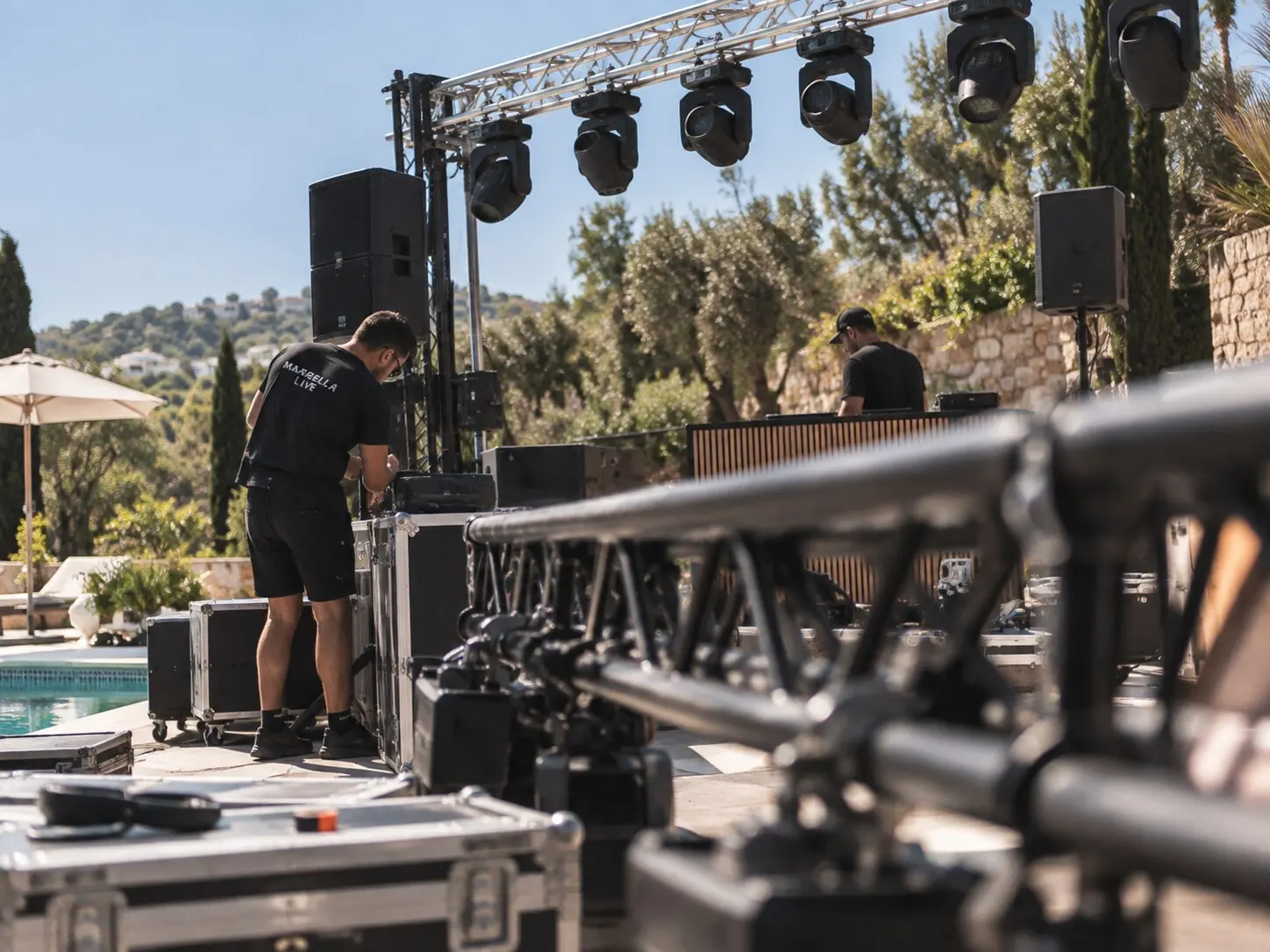 Marbella Live crew rigging truss, moving lights and speakers beside a villa pool during load-in